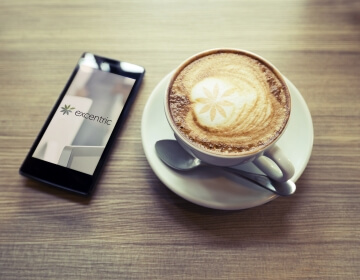 cup of cappuccino on wooden table next to phone displaying excentric website