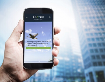 male hand holding phone that displays acaveo website with office towers in background