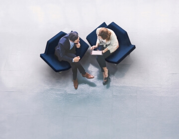 birds eye view of man and woman sitting in blue chairs looking at tablet
