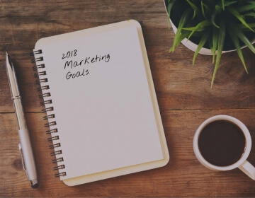 2018 marketing goals on notebook, pen and coffee cup